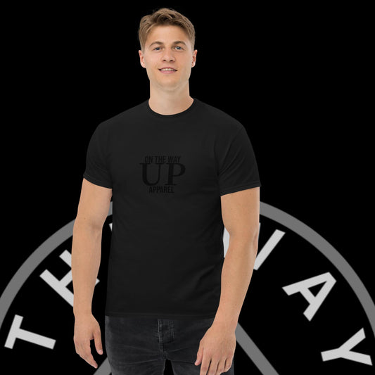 A young man smiling at the camera, wearing a black t-shirt with the text "On The Way Up Apparel" printed in gray. He stands against a background featuring a circular logo with the text "MAX PREMIUM QUALITY.