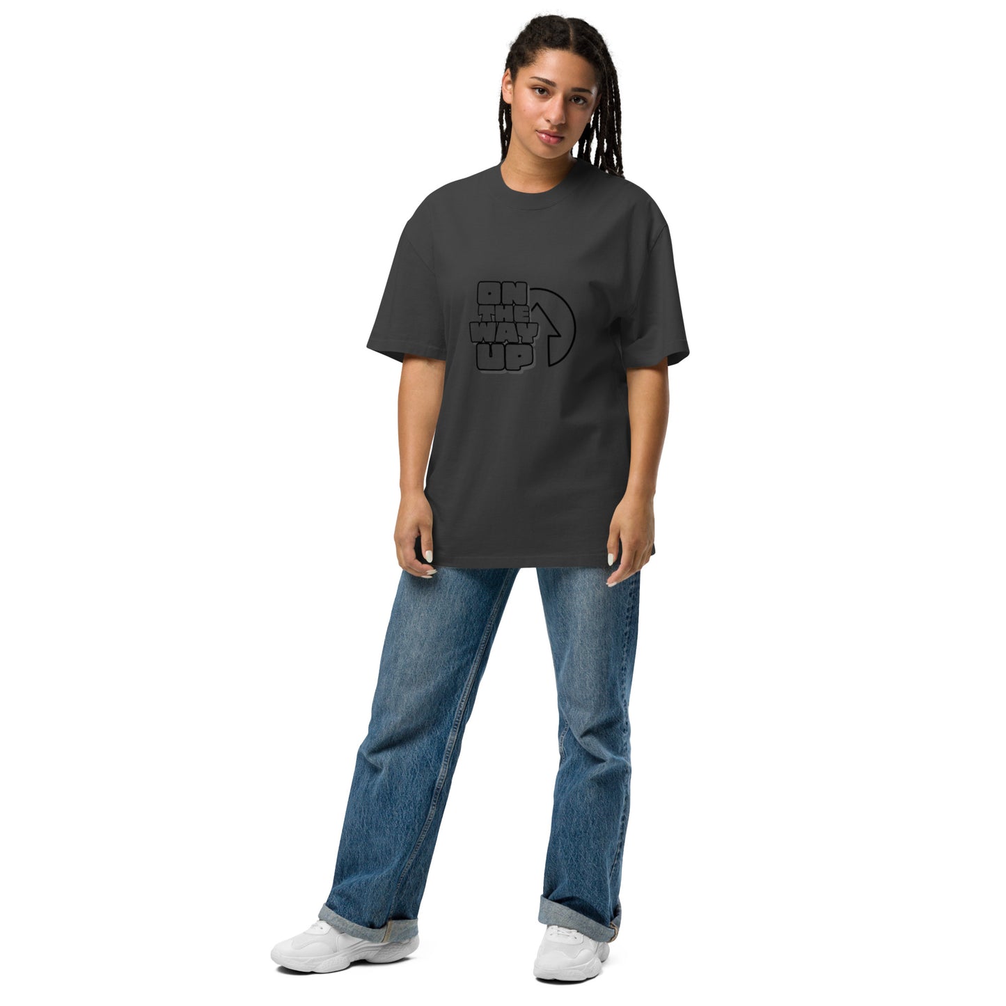 A person in an oversized faded Large print t-shirt from On The Way Up Apparel and jeans stands against a plain white background. Sporting long dreadlocks and white sneakers, they look directly at the camera with a neutral expression.