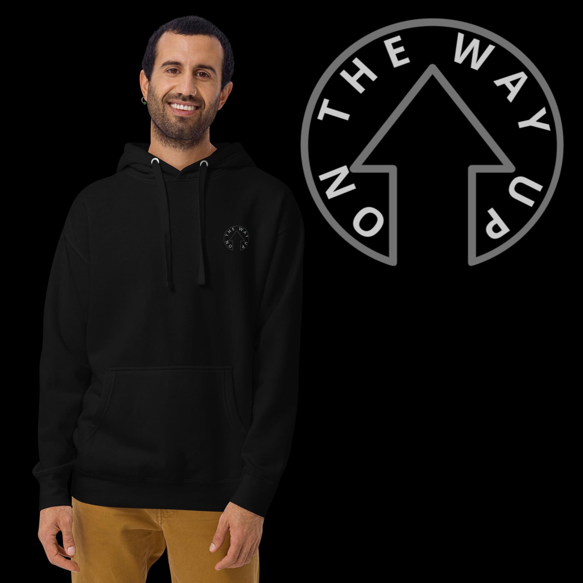 A man smiling, wearing a Signature Hoodie from On The Way Up Apparel with a "Premium Quality" logo on the chest and yellow pants, stands in front of a black background featuring a logo with "THE WAY UP" and an upward arrow.