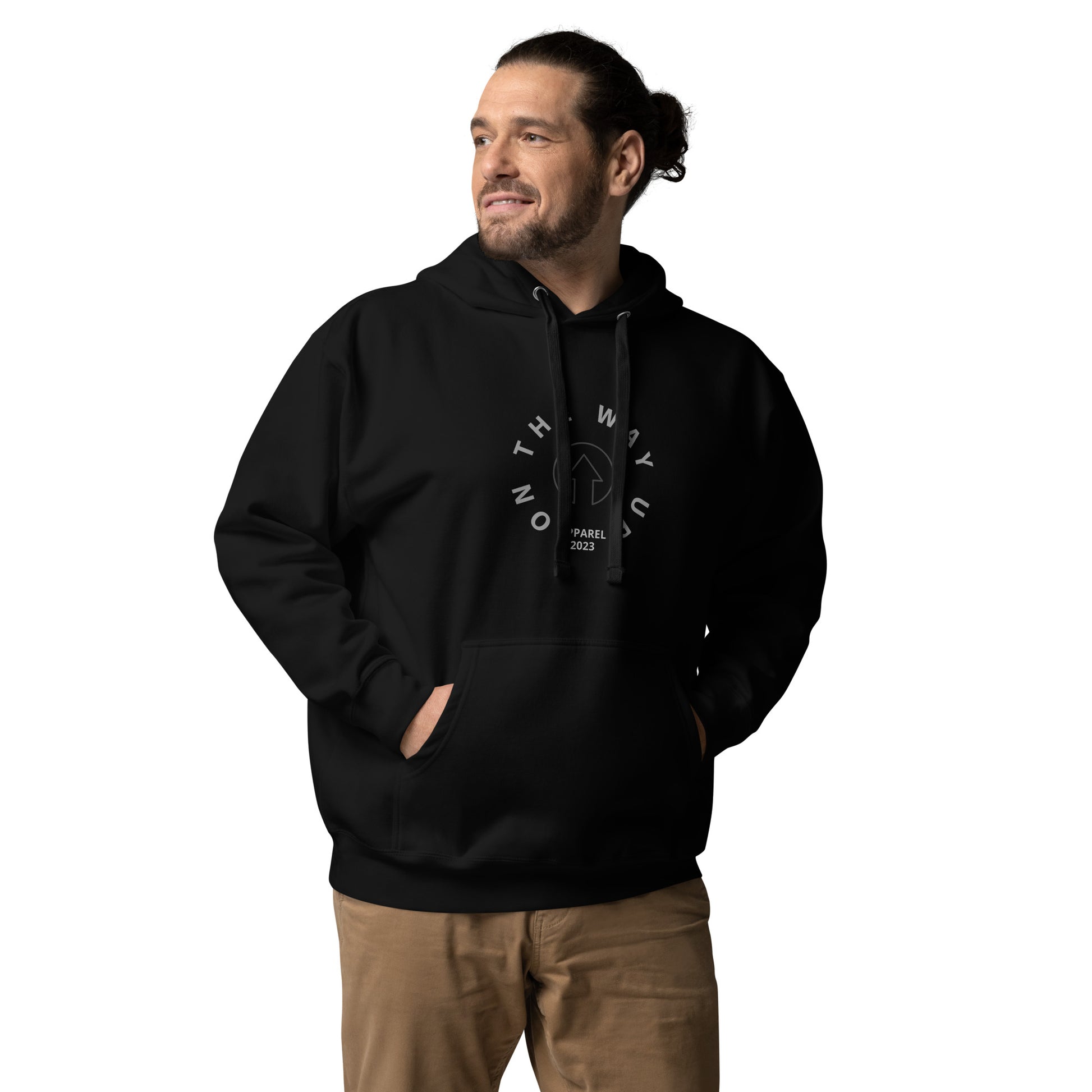 A man wearing a black Vintage Style Hoodie with a white "On The Way Up Apparel" logo on the front and tan pants. He is looking to the side with a slight smile, hands in pockets, embodying the "On The Way Up" spirit.