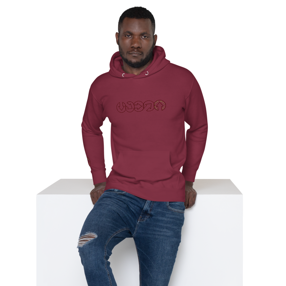 A man in a maroon On The Way Up Progress Hoodie - Cherry and distressed blue jeans sitting on a white block, looking directly at the camera. The hoodie has "Manchester" in a unique text design on the chest.