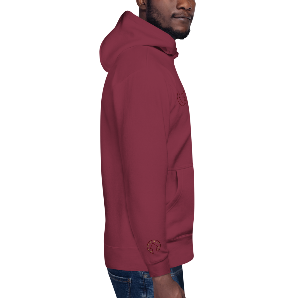 Side view of a young man wearing an On The Way Up Progress Hoodie in Cherry and jeans. The hoodie has the hood up and is embroidered with a logo on the arm.