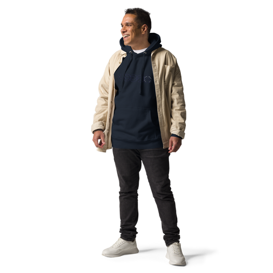 A man standing confidently and smiling, wearing a premium quality cream jacket over the On The Way Up Progress Hoodie in Navy and dark jeans, paired with white sneakers. He is posed against a black background.