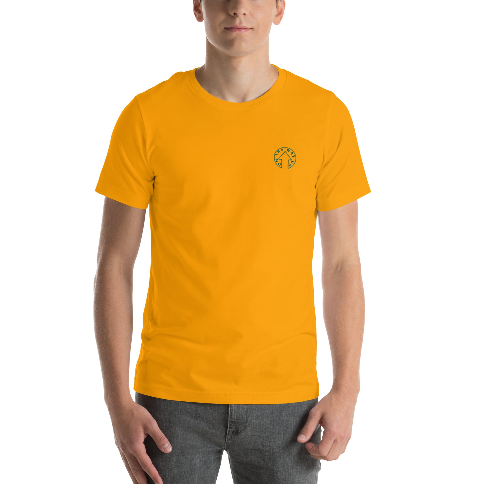 A young man wearing an On The Way Up Apparel BE BOLD - On The Way Up Embroidered Logo T-shirt in yellow and blue jeans stands against a white background, facing the camera with a neutral expression.