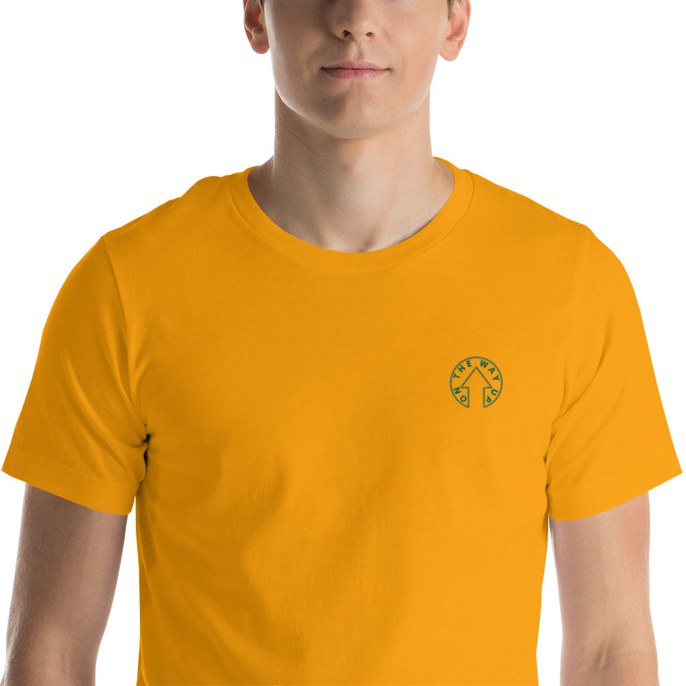 A young man in a BE BOLD - On The Way Up Embroidered Logo T-shirt in YELLOW from On The Way Up Apparel, featuring a small circular "Premium Quality" logo on the left chest, standing against a white background.