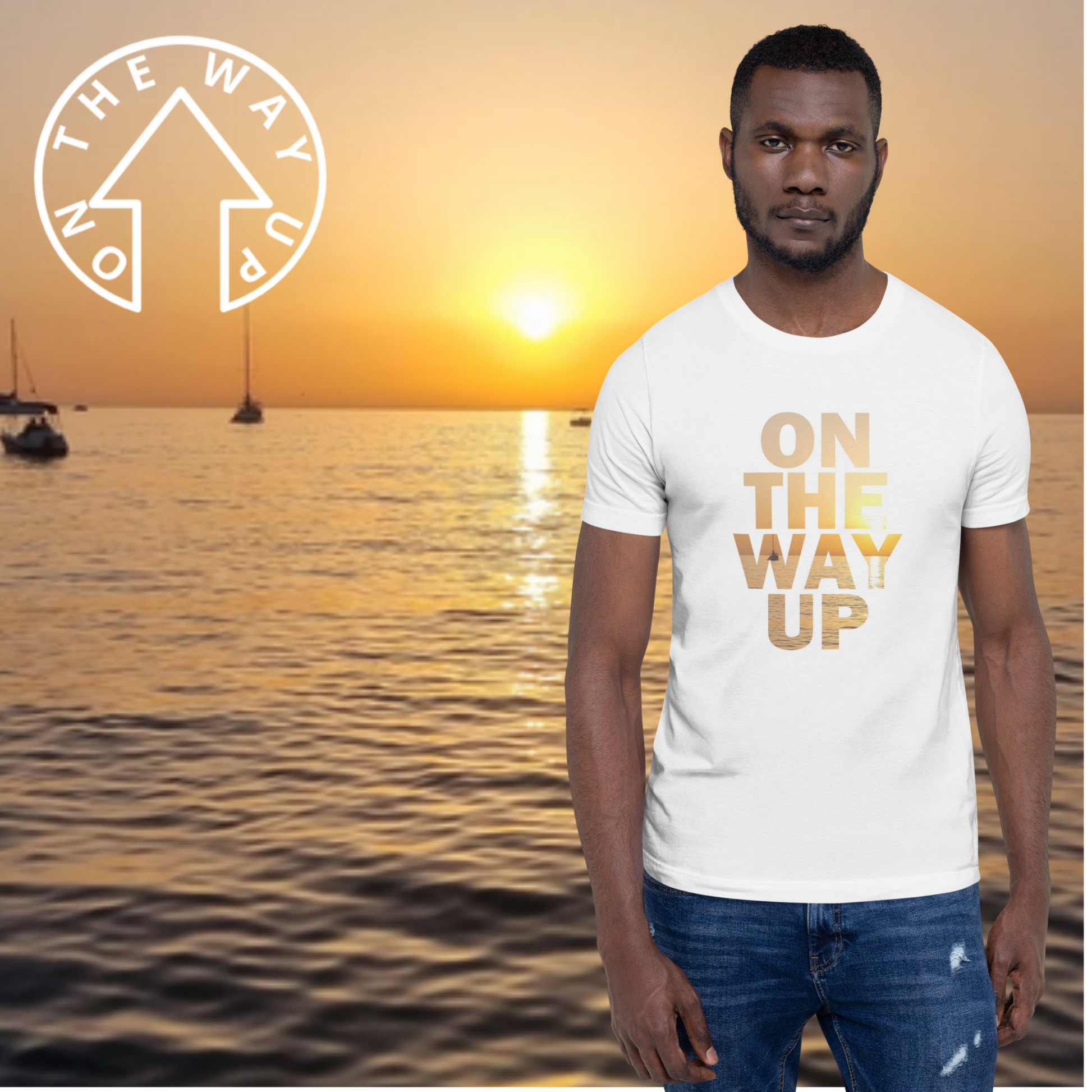 A man stands in front of a serene ocean sunset wearing the Mambo Beach Sunset Tee from On The Way Up Apparel. The lightweight cotton shirt features the words "ON THE WAY UP" printed in gold, with sailboats visible on the water behind him. A circular logo with the same text is positioned in the top left corner of this stylish, pre-shrunk fabric shirt, which is made on demand.