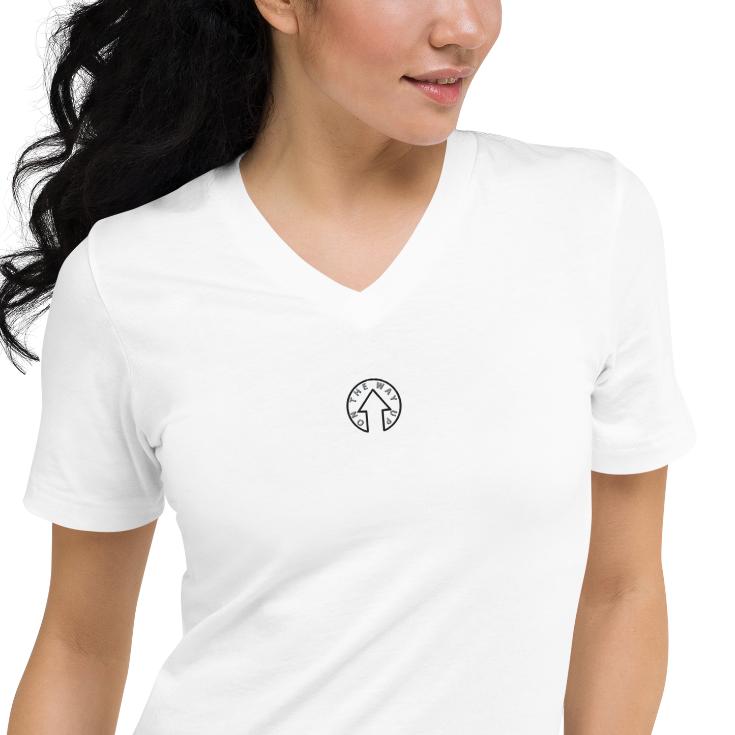 A woman wearing a plain white Signature Short Sleeve V-Neck T-shirt with a small black and white circular "Premium Quality" logo on the left chest area. She has curly dark hair and is looking to her right. Brand name: On The Way Up Apparel